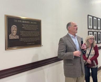 Richard McCord and his wife, Mary (L. to R.) next to the plaque recognizing his 34 years of dedication to Glen Cove, now displayed in City Hall.