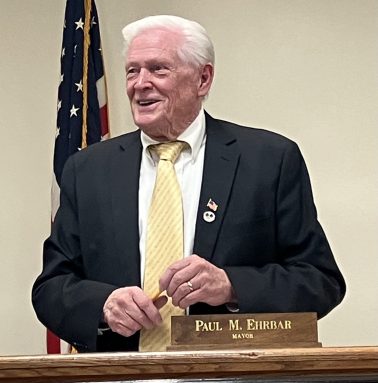 Williston Park Mayor stands and smiles at board table.
