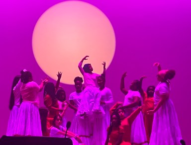 Westbury students pose in a formation on stage in front of purple lighting