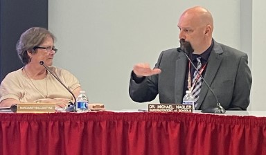 Mineola board members talking, gesturing to each other at board table.