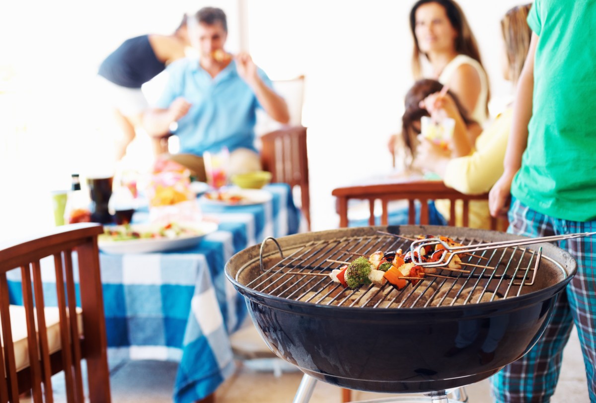 Focus on barbecue with family in background